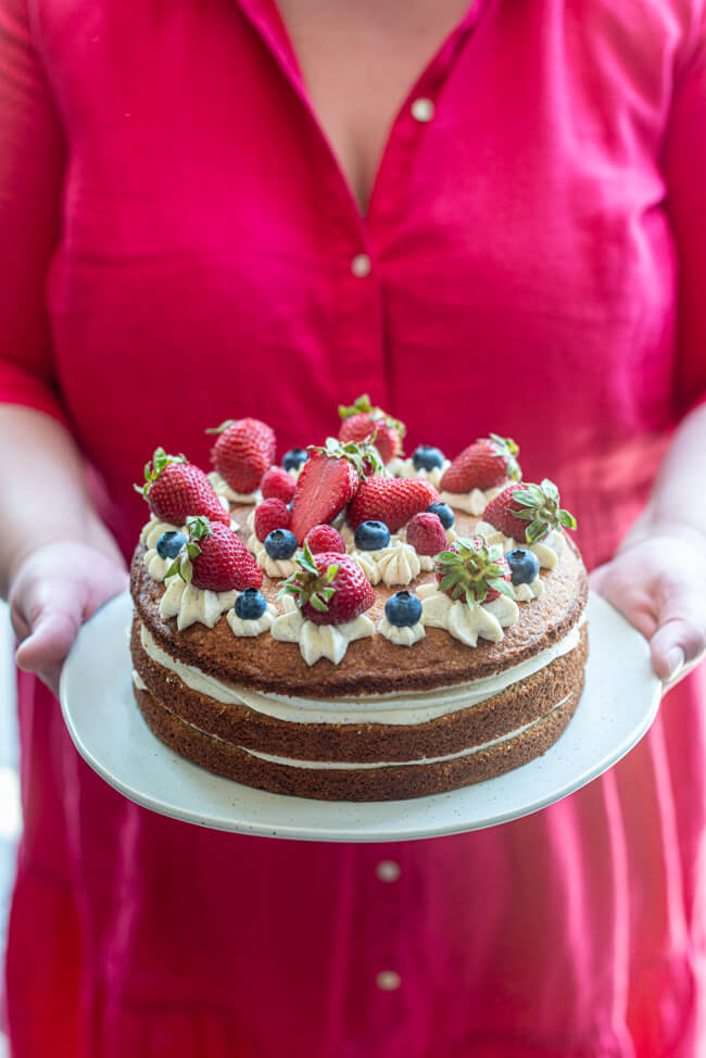 Frau in rotem Kleid hält in ihren Händen einen Teller auf dem die Sommerliche Beerentorte steht.