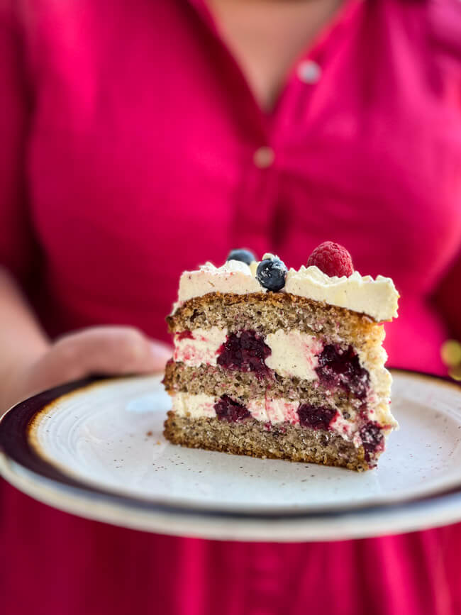 Ein Stück sommerliche Beerentorte auf hellem Teller gehalten von Händen.