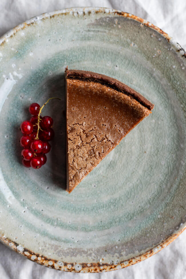 Ein Stück Nougat-Käsekuchen mit Johannisbeer-Rispe auf hellgrünem Keramikteller.