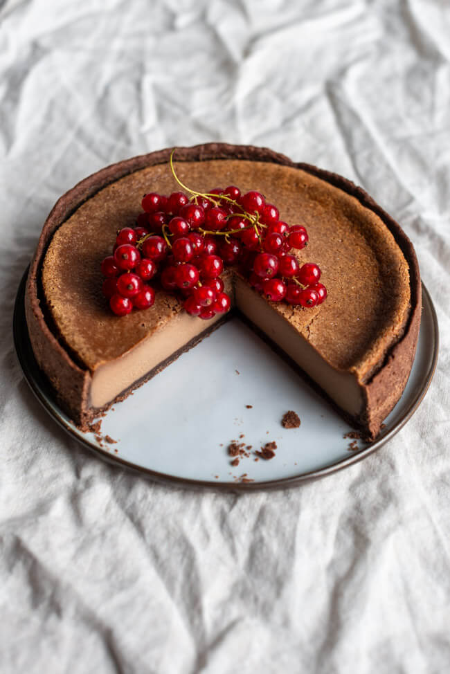 Angeschnittener Nougat-Käsekuchen, dekoriert mit Johannisbeeren auf heller Tischdecke.