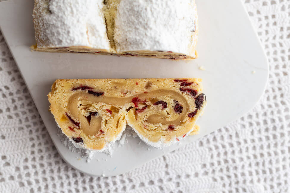 Angeschnittener Marzipanstollen mit Cranberries auf Marmorbrett und weißem Untergrund.
