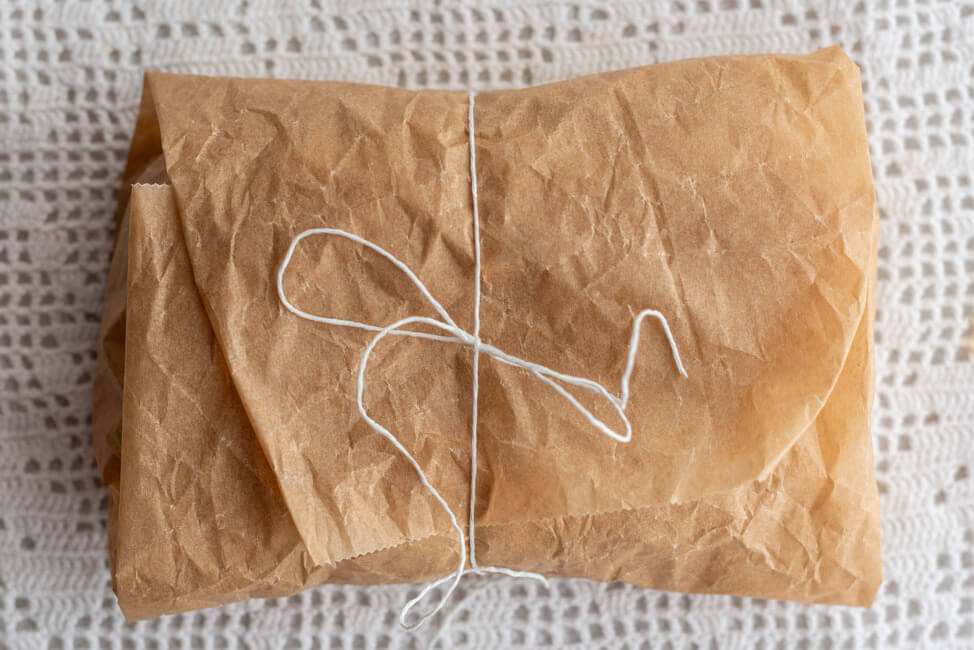 Eingepackter Marzipanstollen mit Cranberries in Backpapier auf hellem Untergrund.