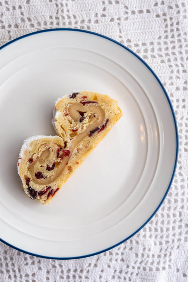 Ein Stück Marzipanstollen mit Cranberries auf weißem Prozellanteller.