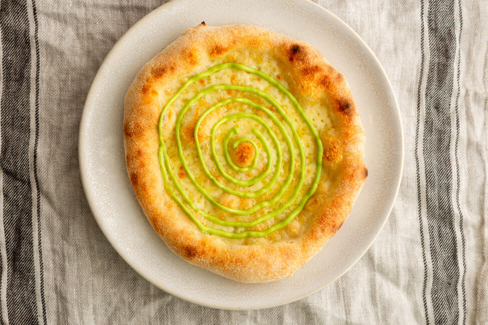 Pizza mit Schnittlauchmayonnaise auf weißem Pizzateller.