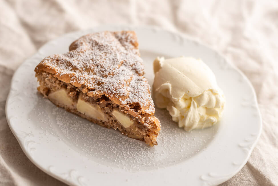 Ein Stück Apfel-Walnuss-Tarte aus Kitchen Impossible mit einem Kleks Sahne auf weißem Teller.