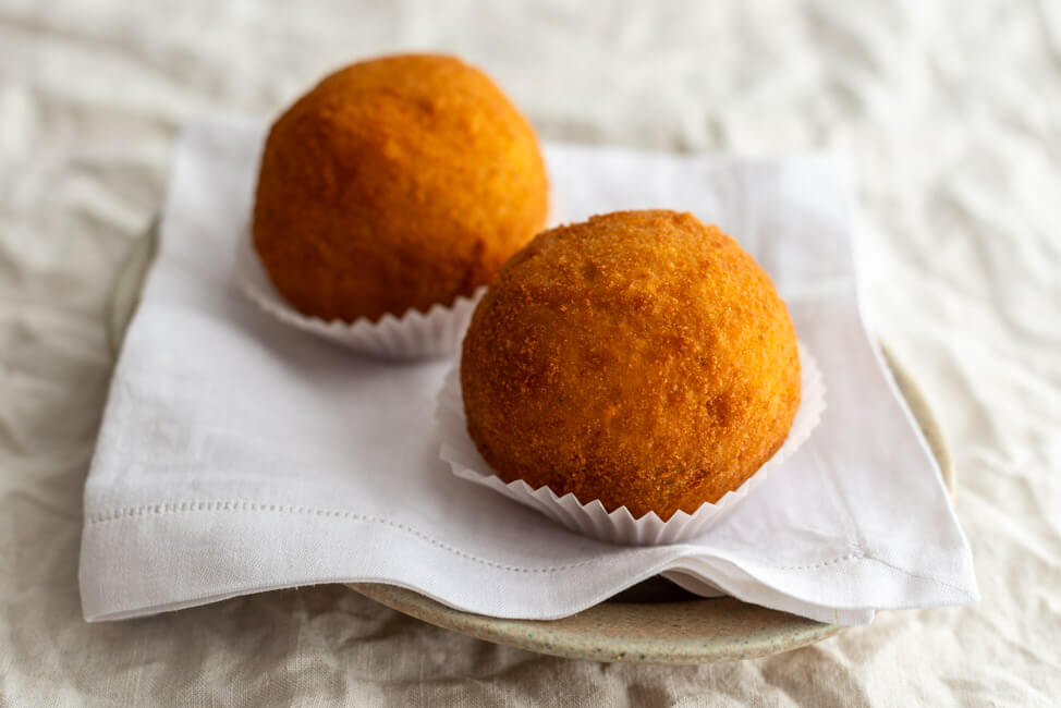 2 Arancini angerichtet auf Teller mit weißer Serviette.