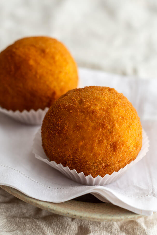 2 Arancini angerichtet auf Teller mit weißer Serviette.