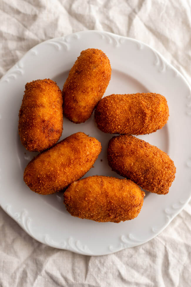 Spanische Kroketten gefüllt mit Schinken und Hähnchen auf weißem Teller.