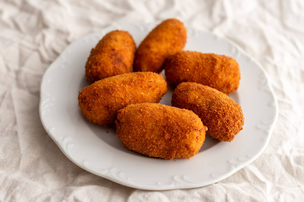 Spanische Kroketten gefüllt mit Schinken und Hähnchen auf weißem Teller.