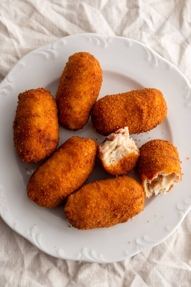 Spanische Kroketten gefüllt mit Schinken und Hähnchen auf weißem Teller.