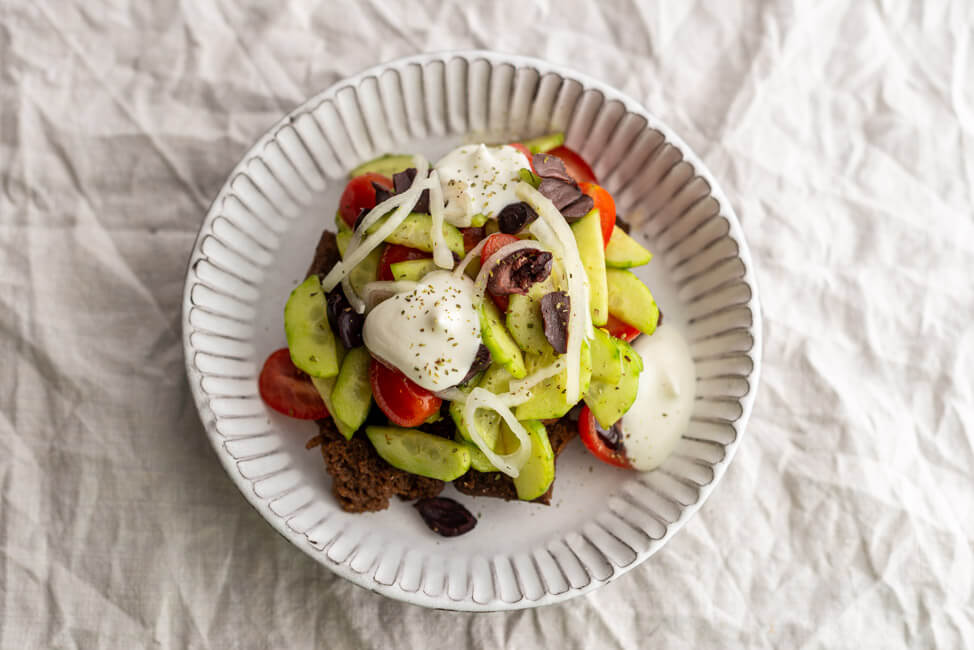 Bauernsalat angerichtet in weißem Tonteller auf hellem Untergrund.