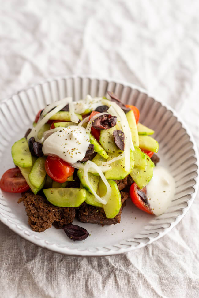 Bauernsalat angerichtet in weißem Tonteller auf hellem Untergrund.