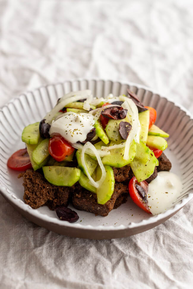 Bauernsalat angerichtet in weißem Tonteller auf hellem Untergrund.