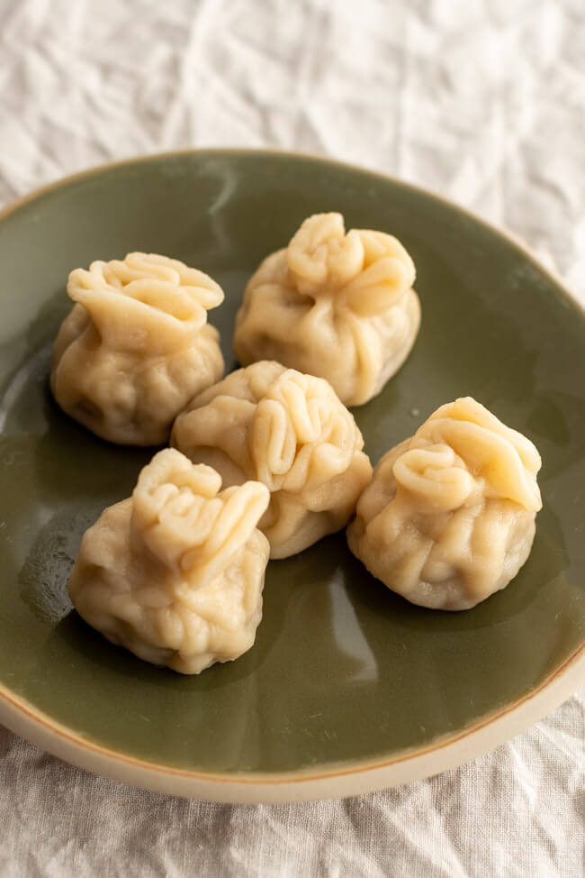 5 Stück Khinkali, angerichtet auf grünem Teller aus Ton.
