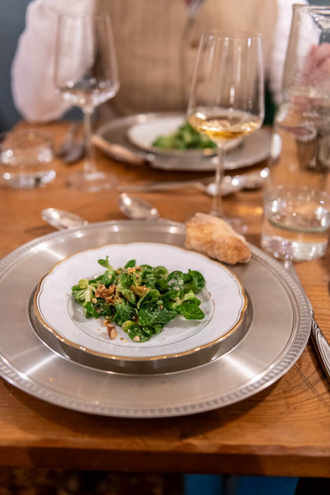 Gedeckter Tisch mit angerichteter Vorspeise: Feldsalat mit Nussvinaigrette und Nusskrokant.
