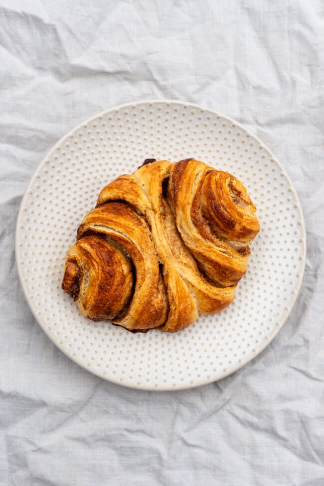 Franzbrötchen auf hellem Porzellanteller und weißem Tischtuch