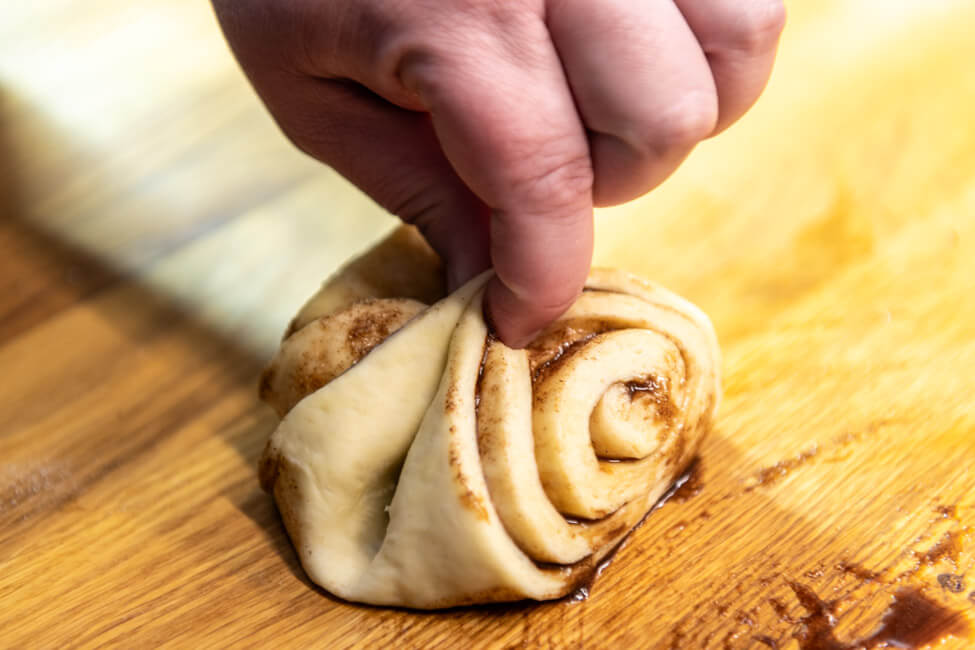 Teig von Franzbrötchen wird mit zwei Fingern zusammengedrückt.