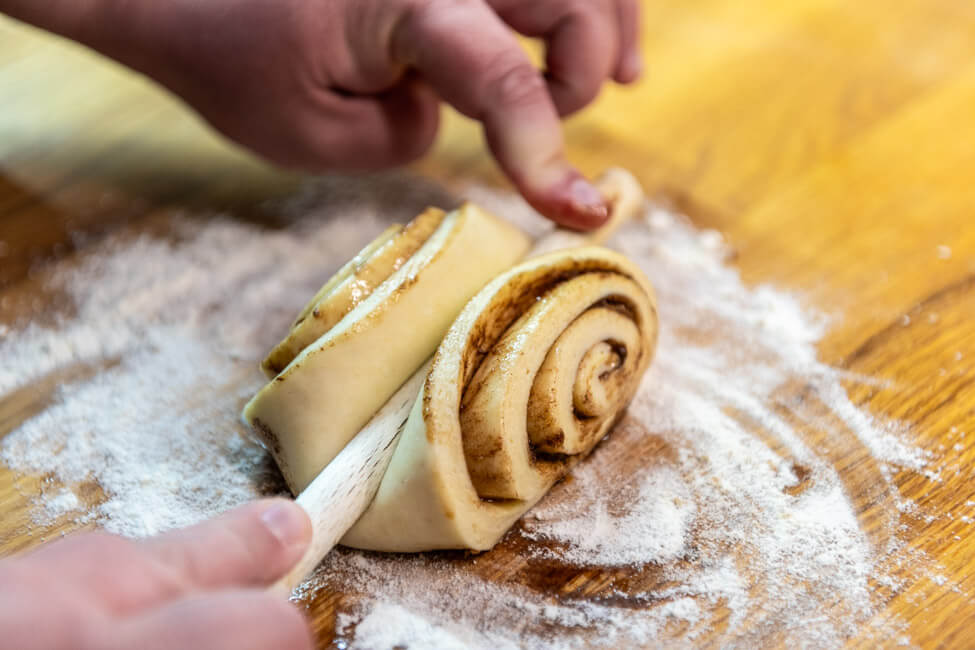 Teigrolle wird mit dem Kochlüffel in die typische Franzbrötchen Form gebracht.