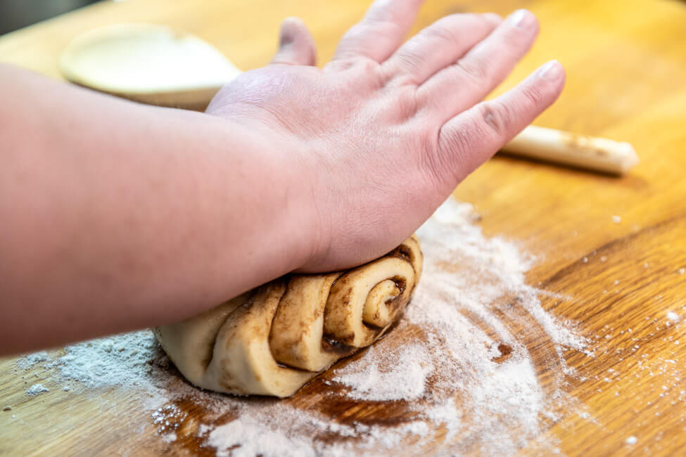 Franzbrötchen wird mit der Handfläche flach gedrückt.
