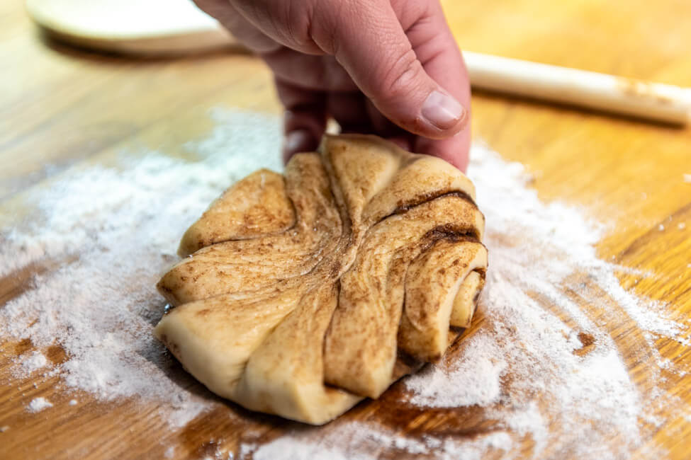 Flachgedrüktes Franzbrötchen wird mit Hand von Holzbrett gehoben.