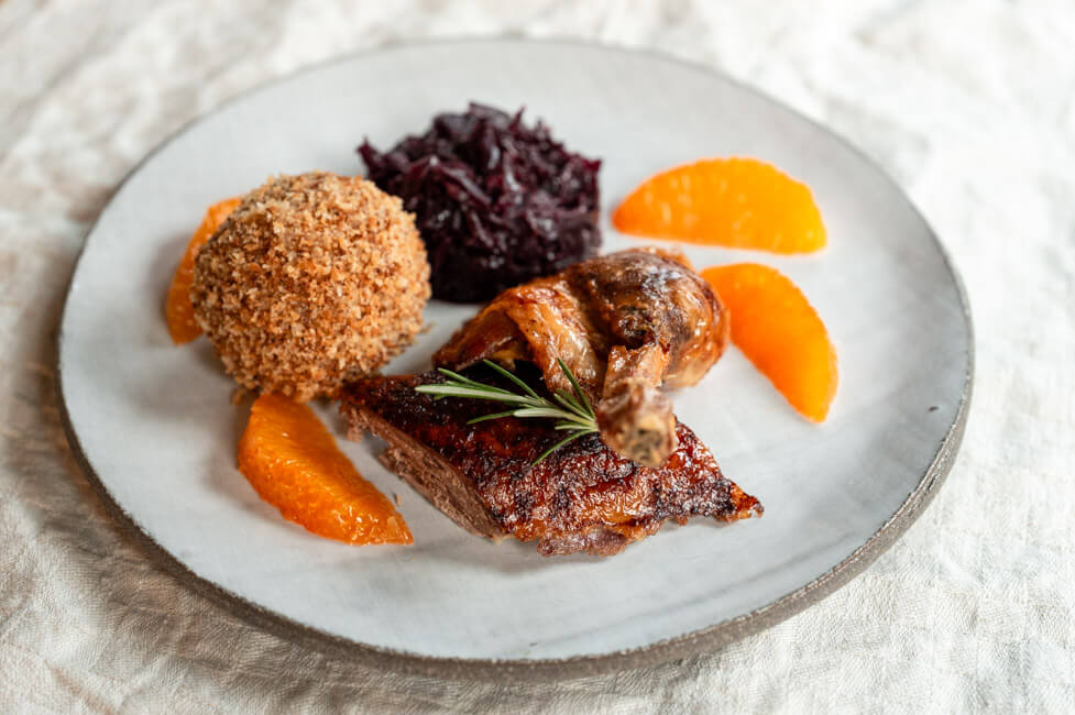 Bauernernte mit Klößen, Rotkohl aus Kitchen Impossible auf hellem Teller und cremefarbener Tischdecke.