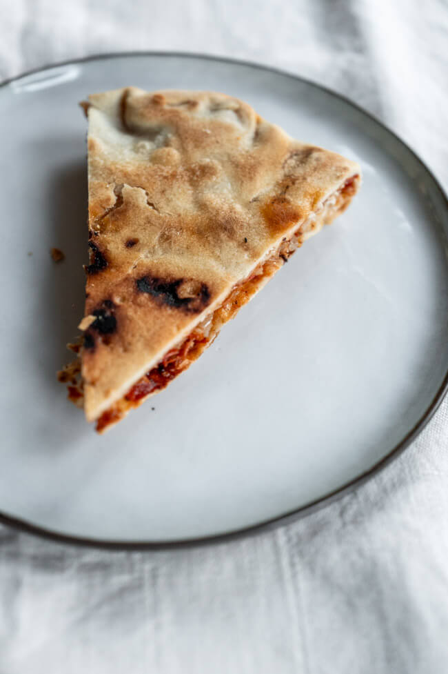 Byrek mit Zwiebeln und Tomate auf schwarzem Teller
