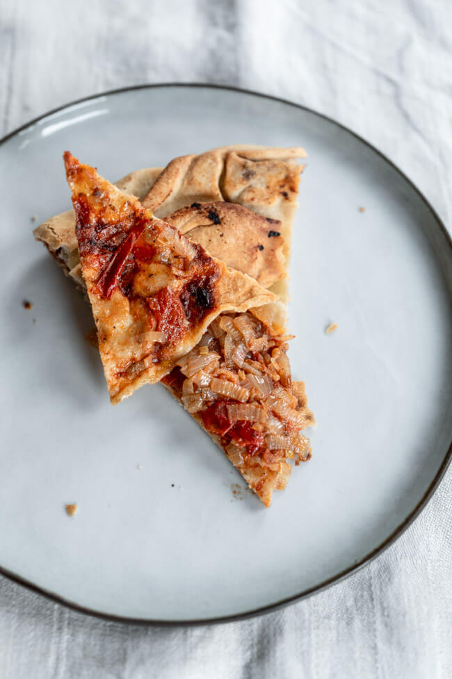 Byrek mit Zwiebeln und Tomate auf schwarzem Teller