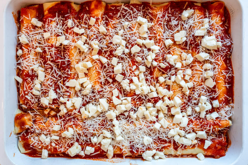 Frisch gefüllte Cannelloni im Backblech auf Tomatensauce mit Käse bestreut vor dem Backen