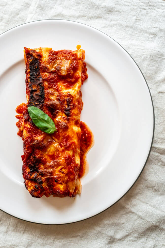 Zwei Canneloni auf weißem Porzellanteller mit einem Blatt Basilikum garniert