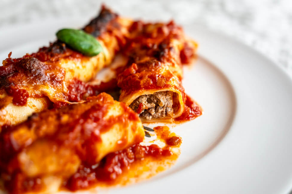 Zwei Canneloni auf weißem Porzellanteller mit einem Blatt Basilikum garniert