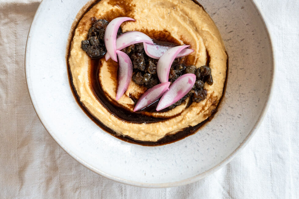 Fava mit Kapern-Marmelade und gepickelten Zwiebeln in weißem Teller