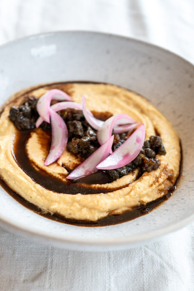 Fava mit Kapern-Marmelade und gepickelten Zwiebeln in weißem Teller