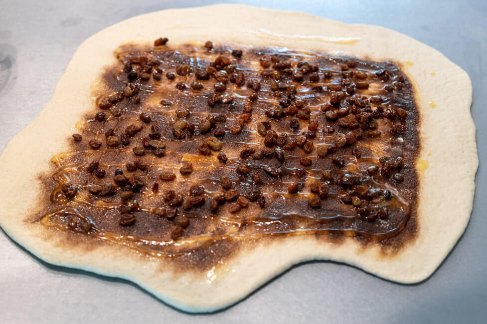 Ausgerollter Hefeteig mit Honig, Zucker, Butter, Zimt und Rosinen