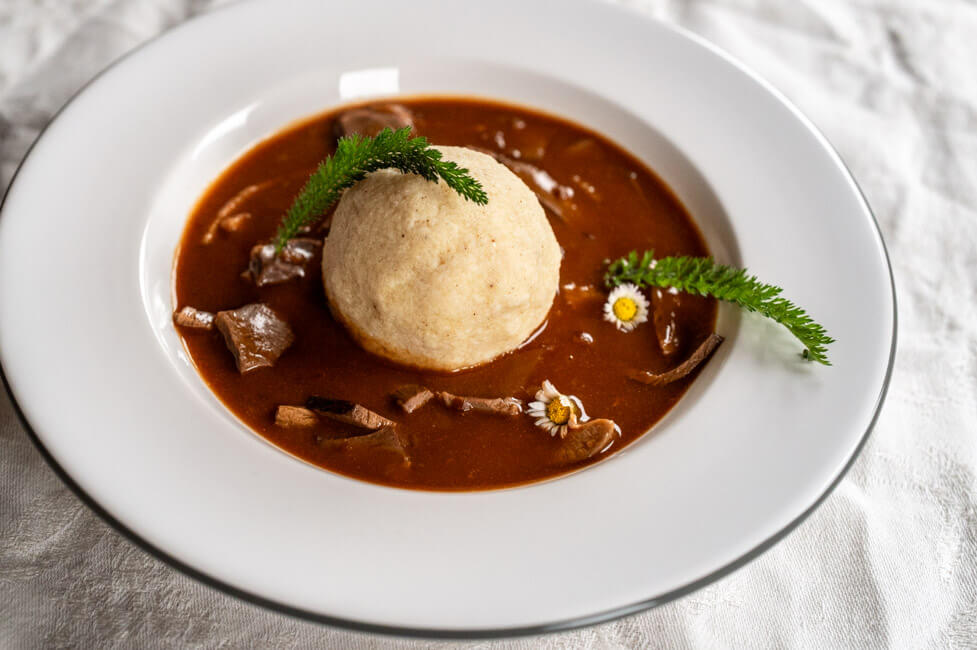 Kalbsrahmbeuschel mit Grießknödel angerichtet in weißem Teller mit Gänseblümchen und Schafgarbe