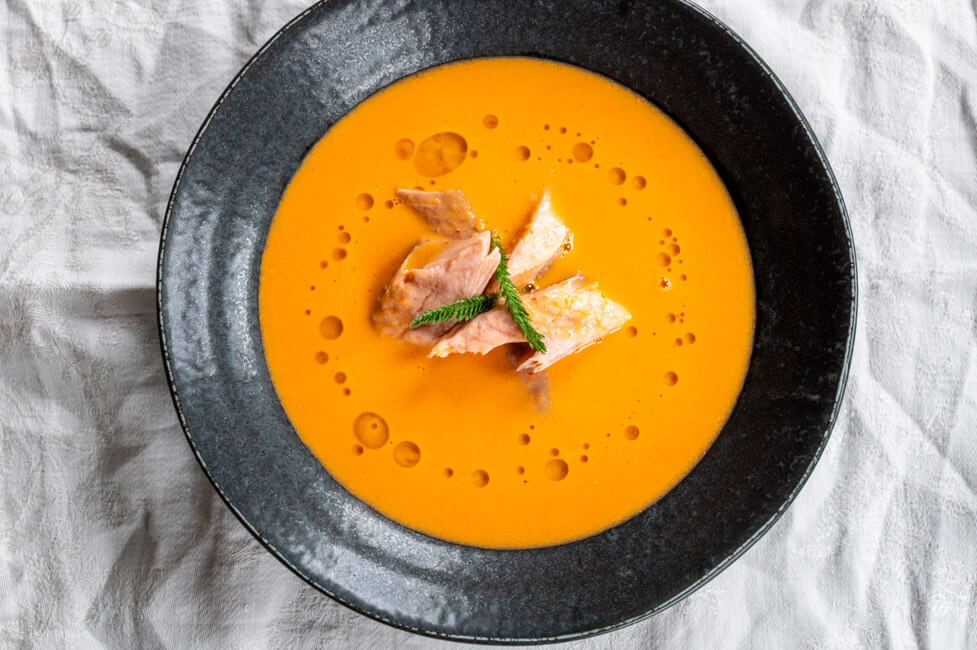 Paradeiser-Ingwer-Kokosschaumsuppe mit geräuchertem Fisch in schwarzem Teller