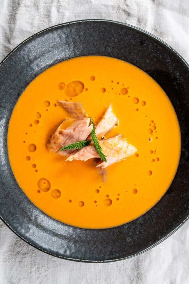 Paradeiser-Ingwer-Kokosschaumsuppe mit geräuchertem Fisch in schwarzem Teller