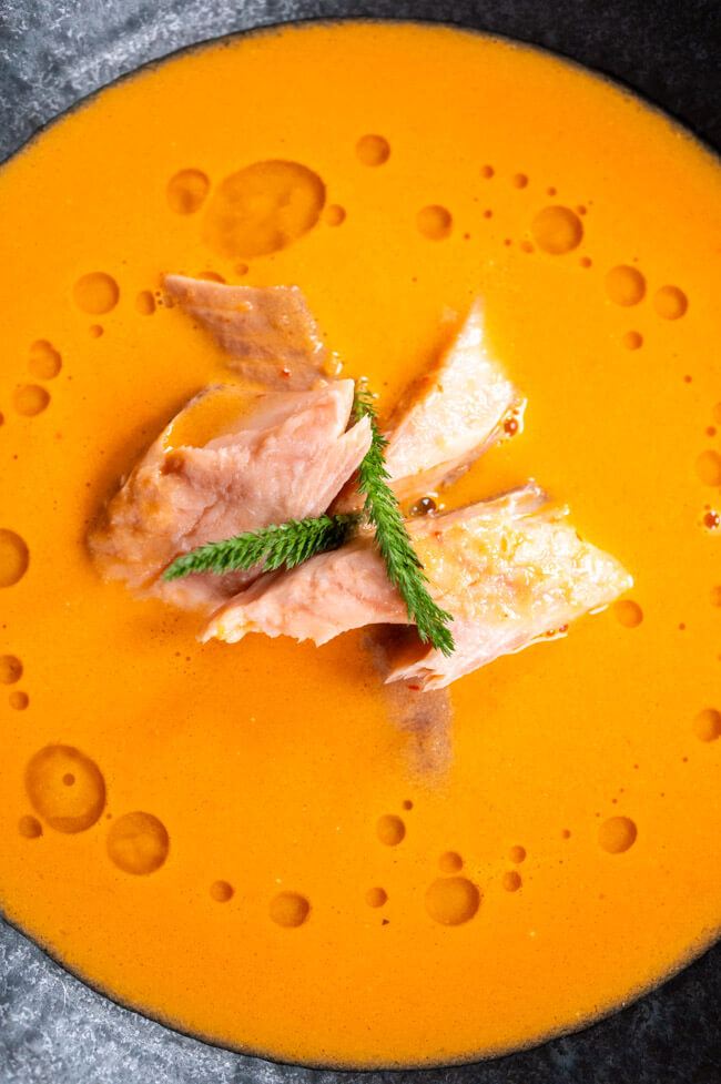 Tomatensuppe mit geräuchertem Fisch in schwarzem Teller