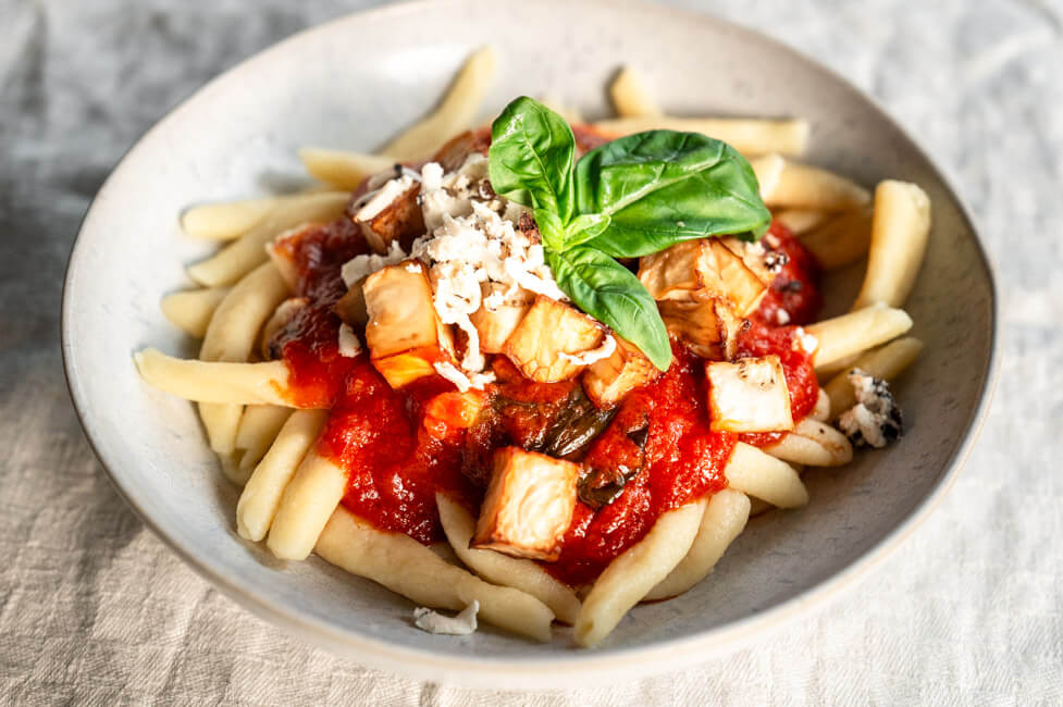 Pasta alla Norma mit frischem Basilikum in weißem Teller angerichtet