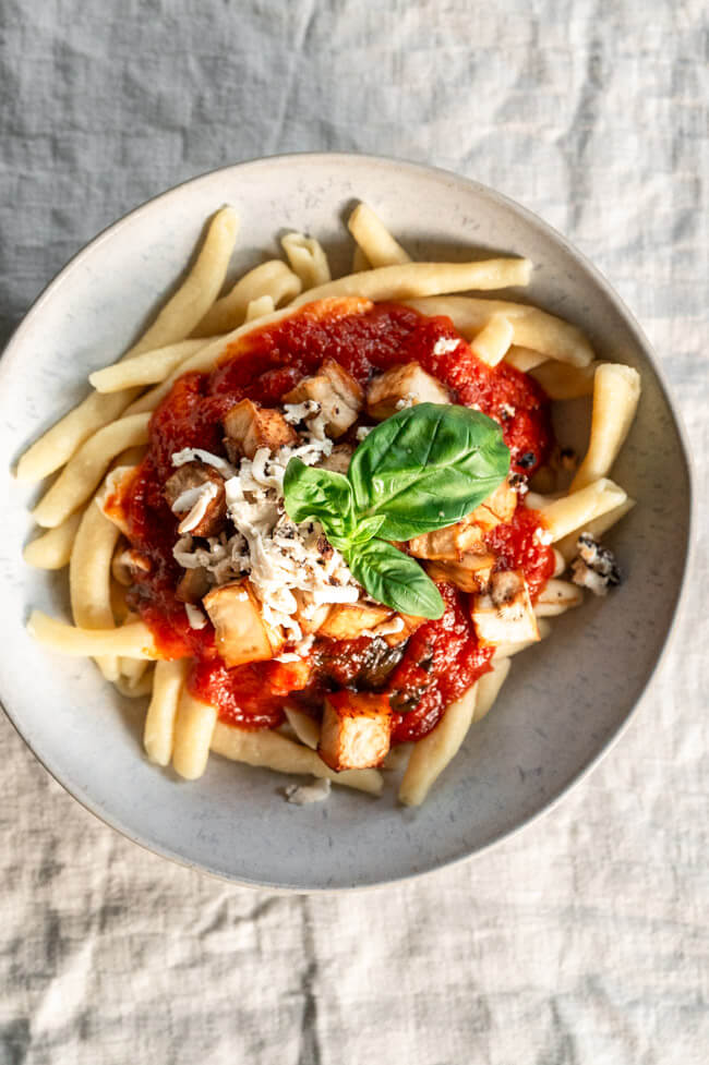 Maccheroni alla Norma mit frischem Basilikum in weißem Teller angerichtet
