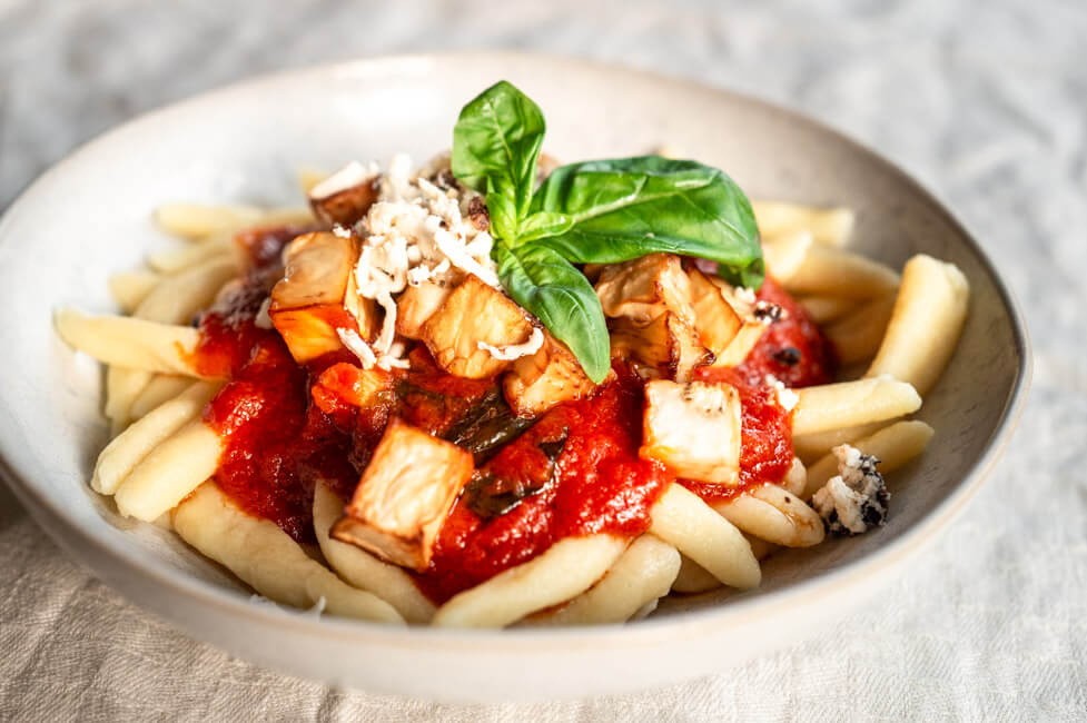 Maccheroni alla Norma mit frischem Basilikum in weißem Teller angerichtet