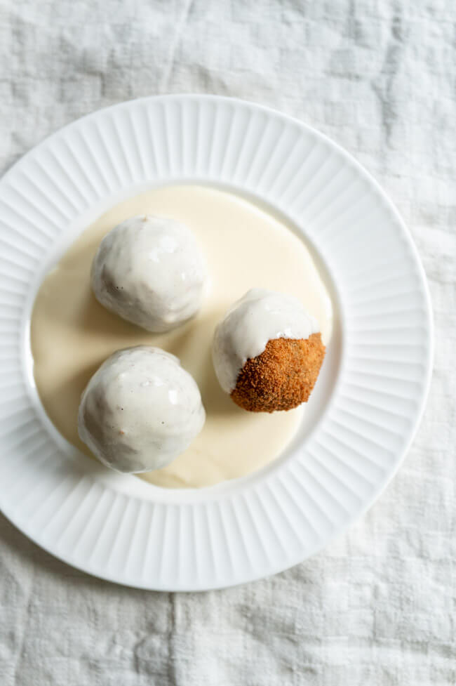 3 Polpette mit wildem Brokkoli und weißer Käsesoße auf weißem Teller