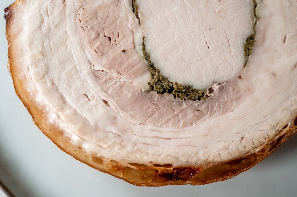 Eine Scheibe Porchetta abgekühlt auf hellem Teller