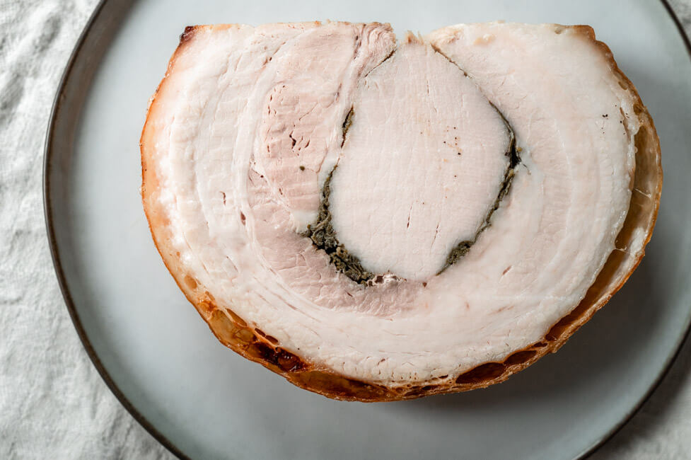 Eine Scheibe Porchetta abgekühlt auf hellem Teller