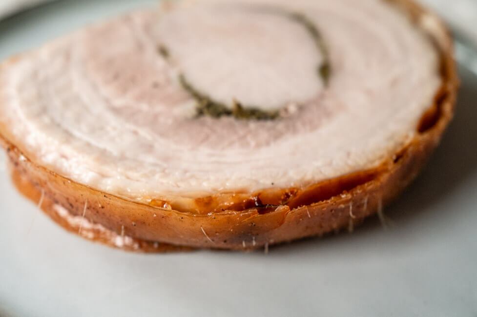Eine Scheibe Porchetta abgekühlt auf hellem Teller