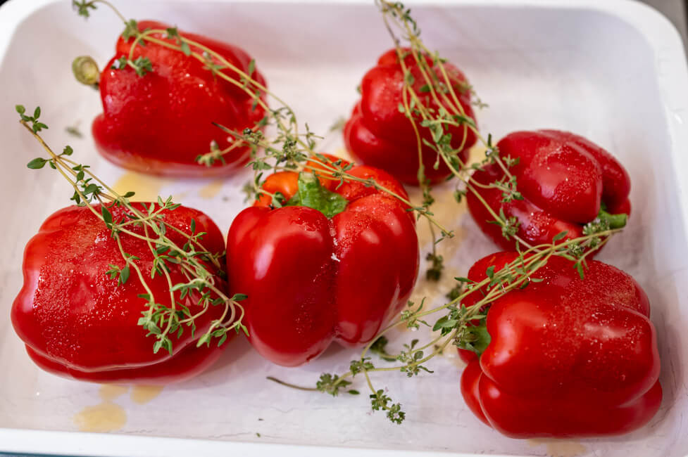 5 rote Paprika mit Olivenöl, Salz und Thymian auf Backblech.