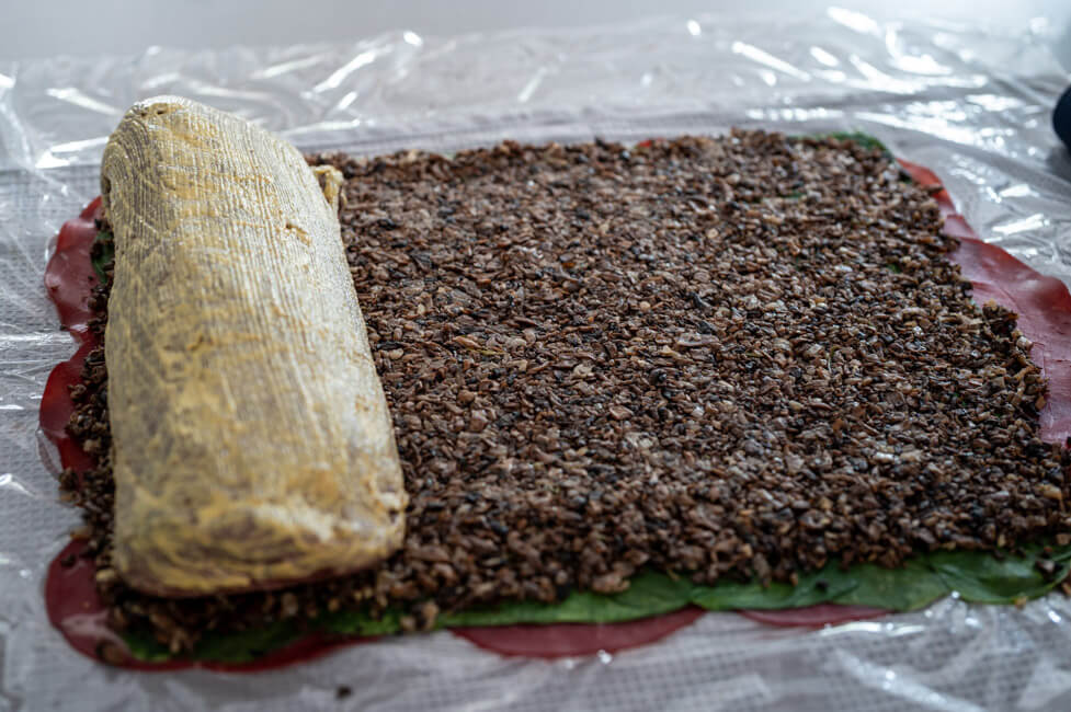Rinderfilet mit Senf bestrichen liegt auf Bresaola, Spinat und Duxelles Schicht