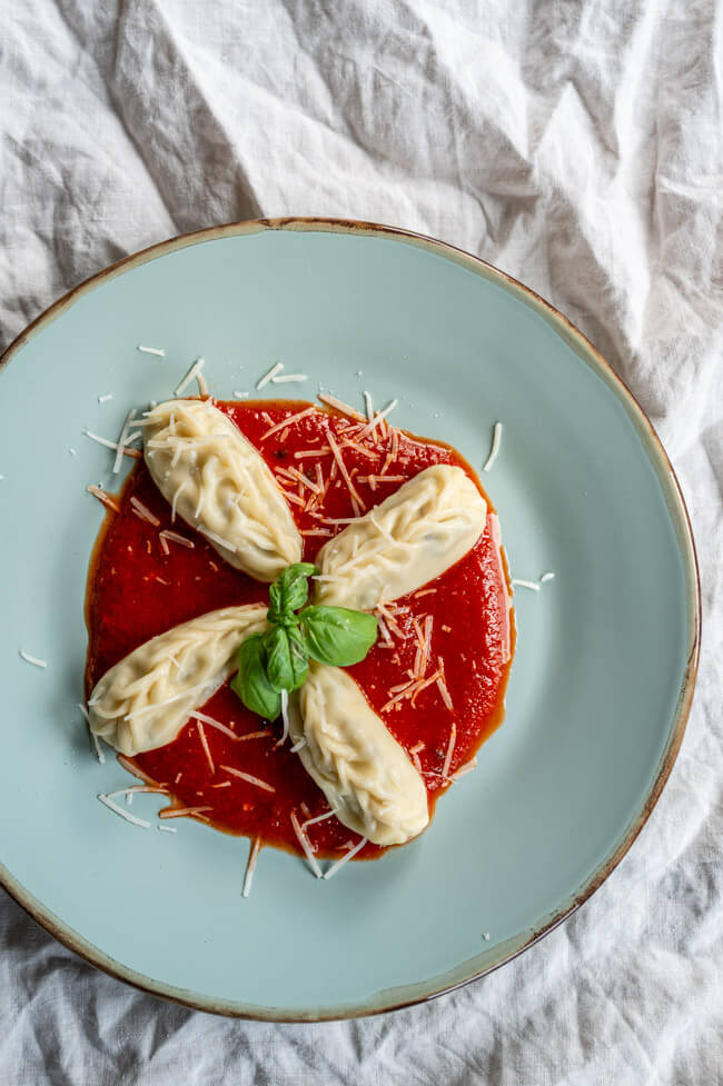 4 Culurgiones mit Tomatensauce, Parmesan und frischem Basilikum auf blauem Teller angerichtet