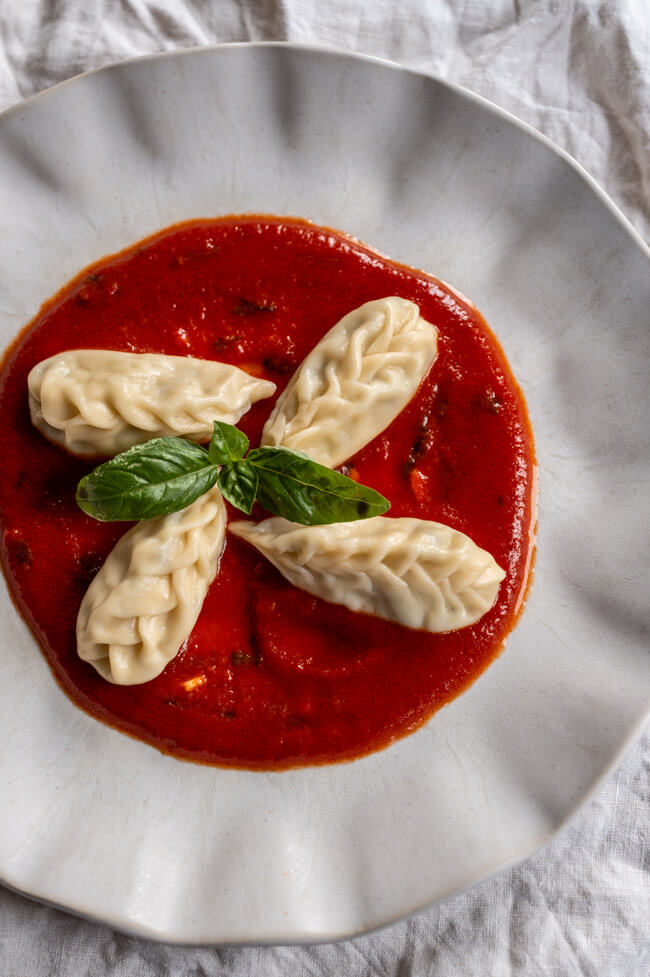 4 Culurgiones mit Tomatensauce und frischem Basilikum auf hellem Teller angerichtet