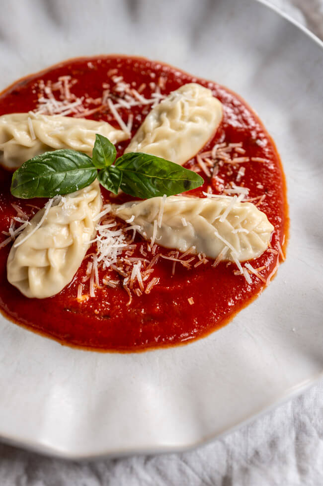 4 Culurgiones mit Tomatensauce, Parmesan und frischem Basilikum auf hellem Teller angerichtet