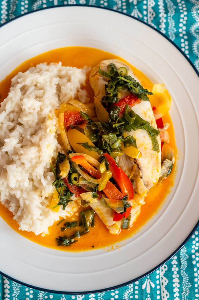 Moqueca de peixe mit Reis auf weißem Teller angerichtet auf blauem Tischtuch